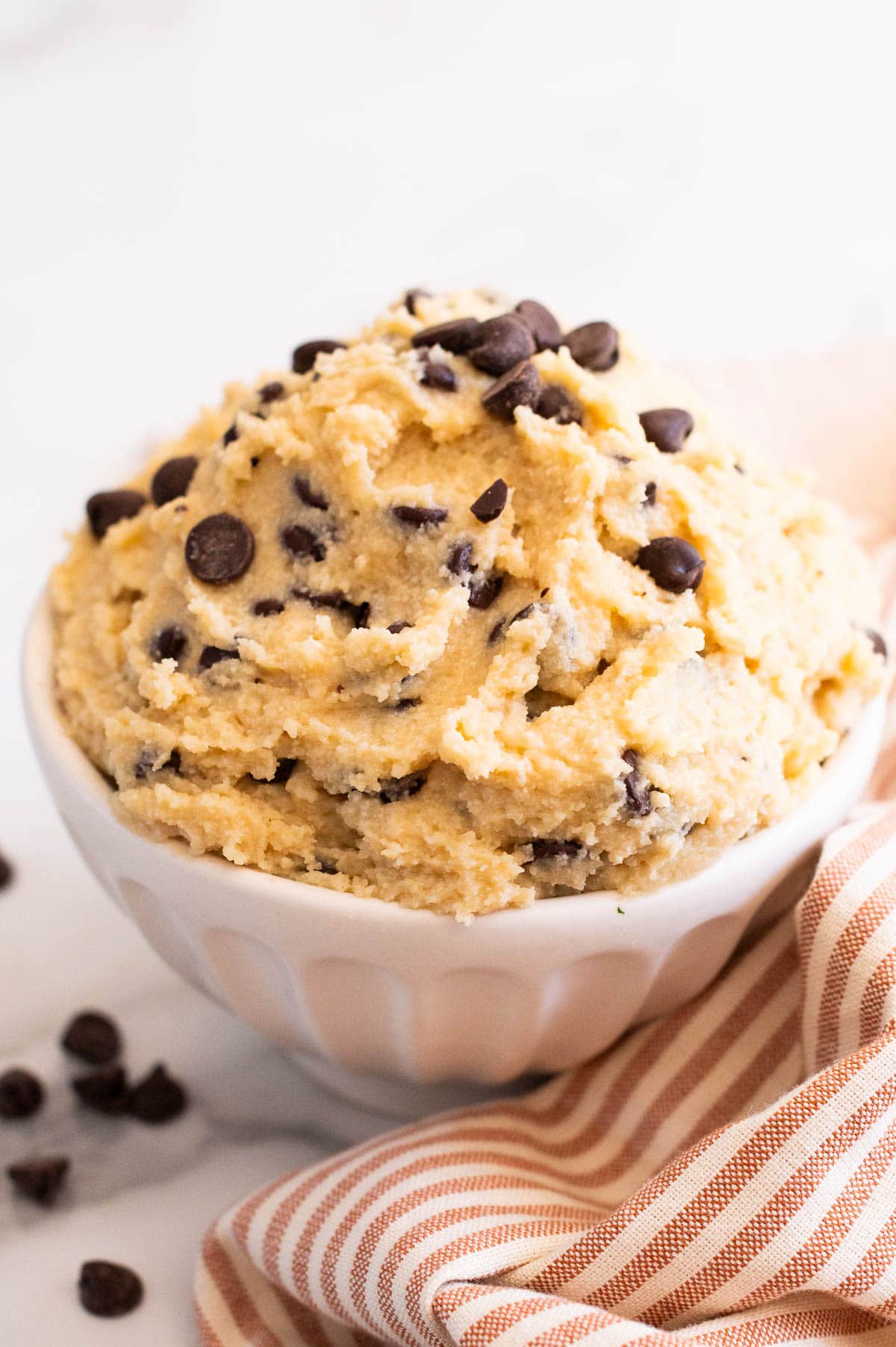 Cottage cheese cookie dough in a bowl. Linen towel and chocolate chips on a counter.