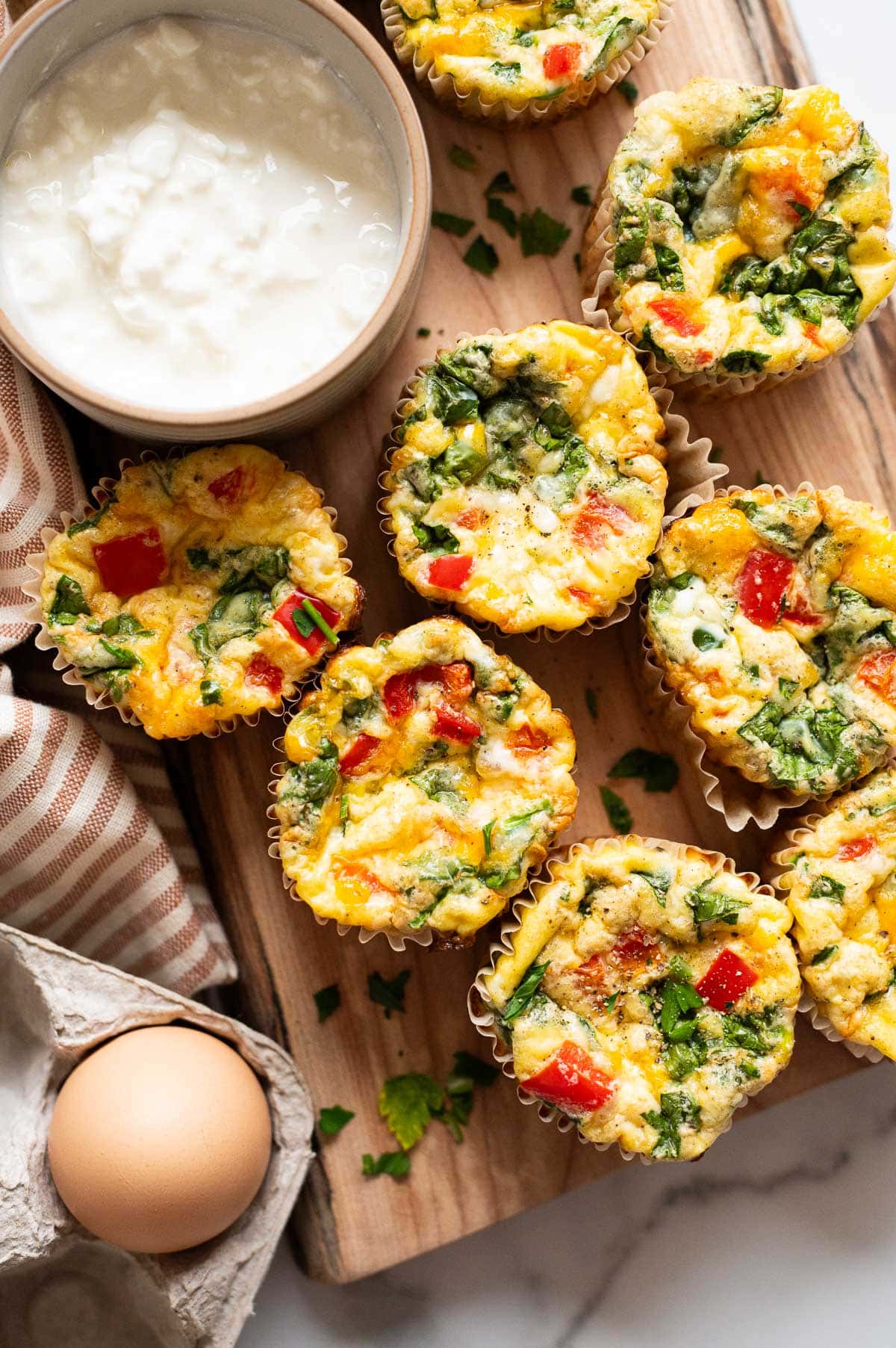 Cottage cheese egg muffins on a wooden board with a bowl of cottage cheese, egg and napkin.