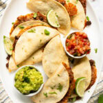 Baked tacos served with guacamole and pico de gallo on a platter.