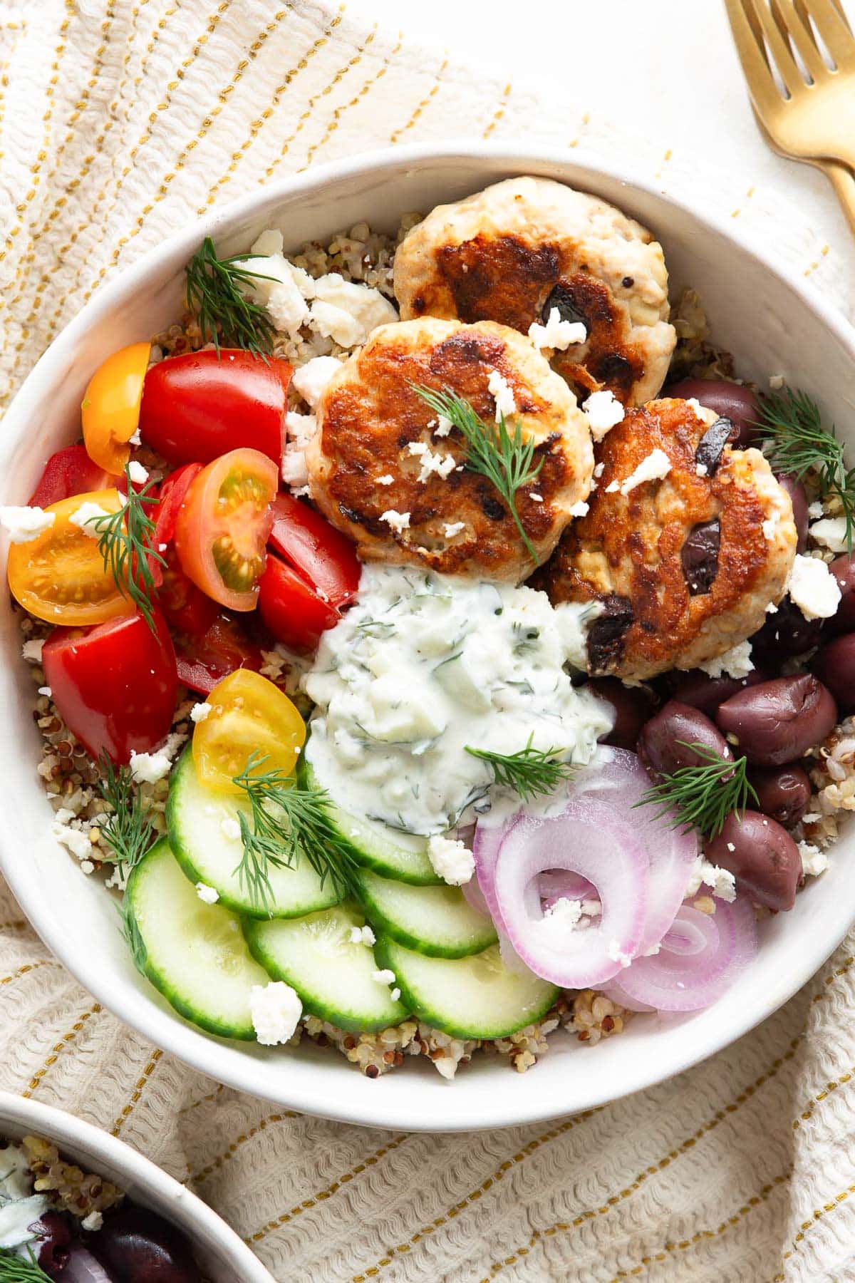 Greek turkey burgers served in a bowl with quinoa, vegetables and tzatziki.