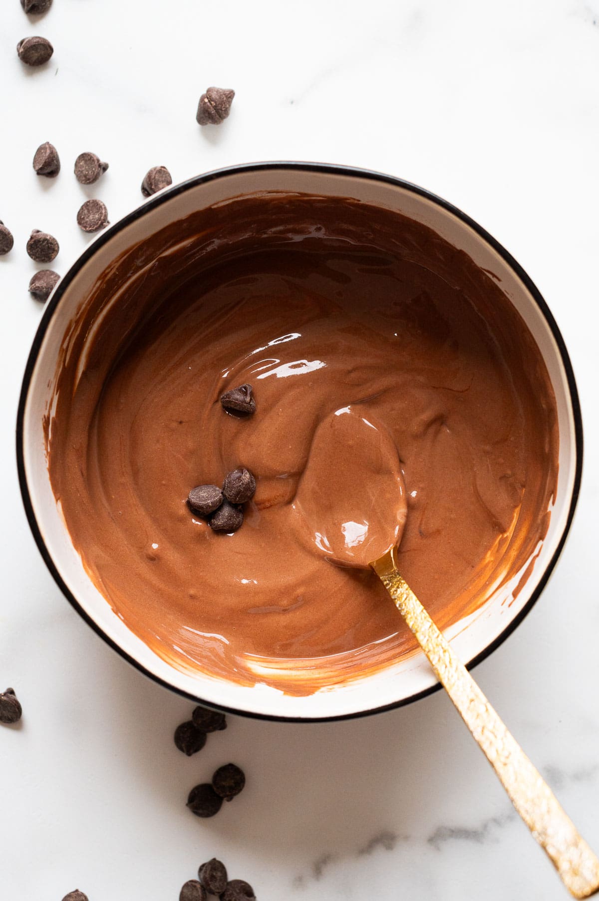 Greek yogurt chocolate pudding with chocolate chips in a bowl with a spoon.