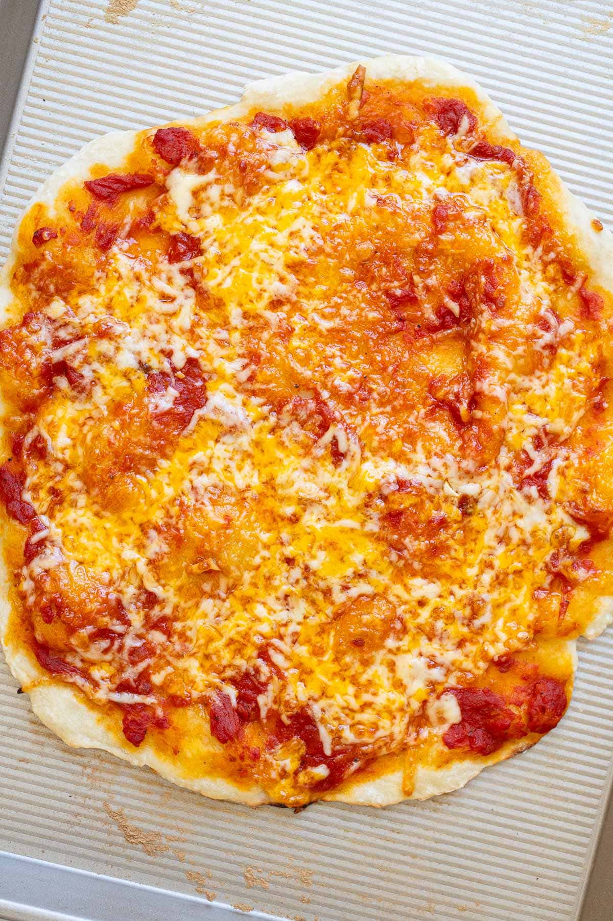 Greek yogurt pizza crust with marinara and cheese on a baking sheet.