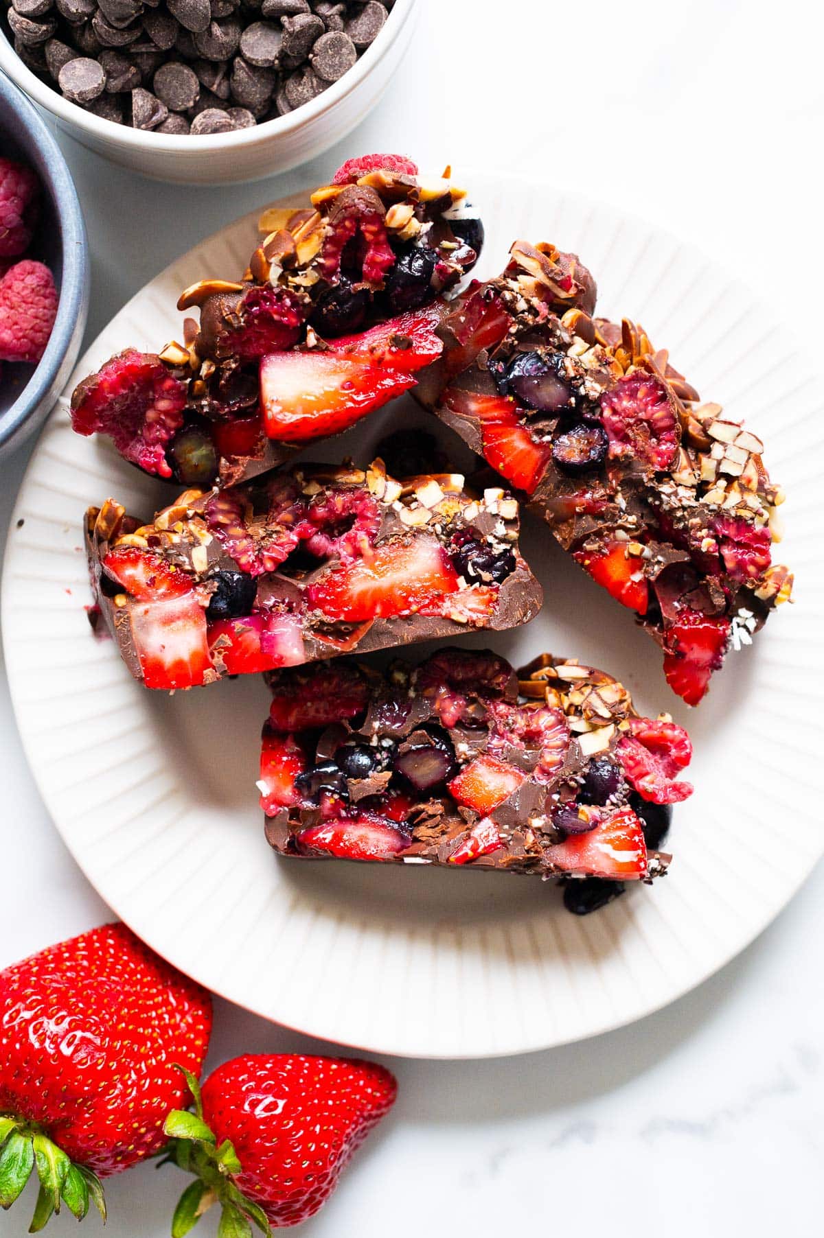 Four chocolate berry bars on a plate. Chocolate chips, raspberries and strawberries on the counter.