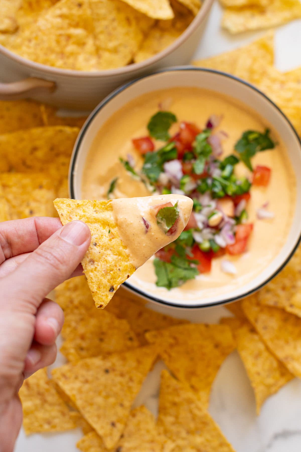 Person holding a chip dipped into a queso dip.