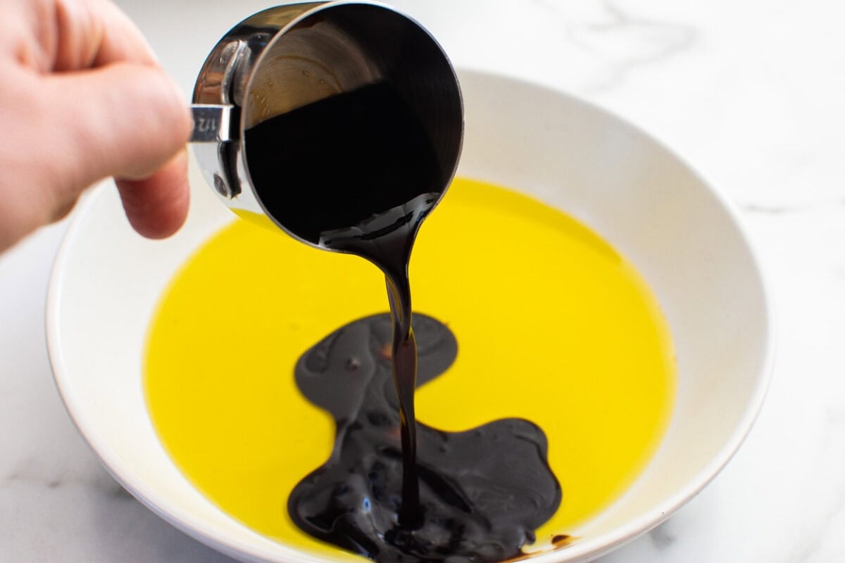 Person pouring balsamic vinegar into a bowl with olive oil.