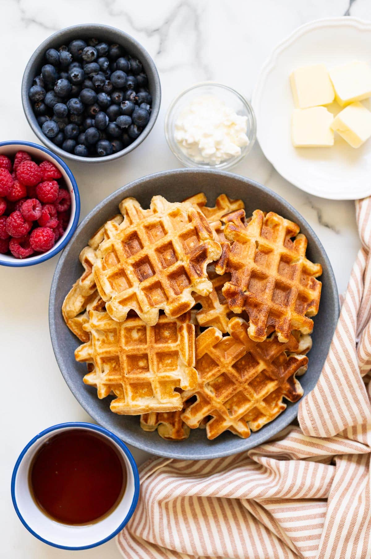 Cottage cheese waffles in a bowl. Butter, berries, cottage cheese and maple syrup in bowls.