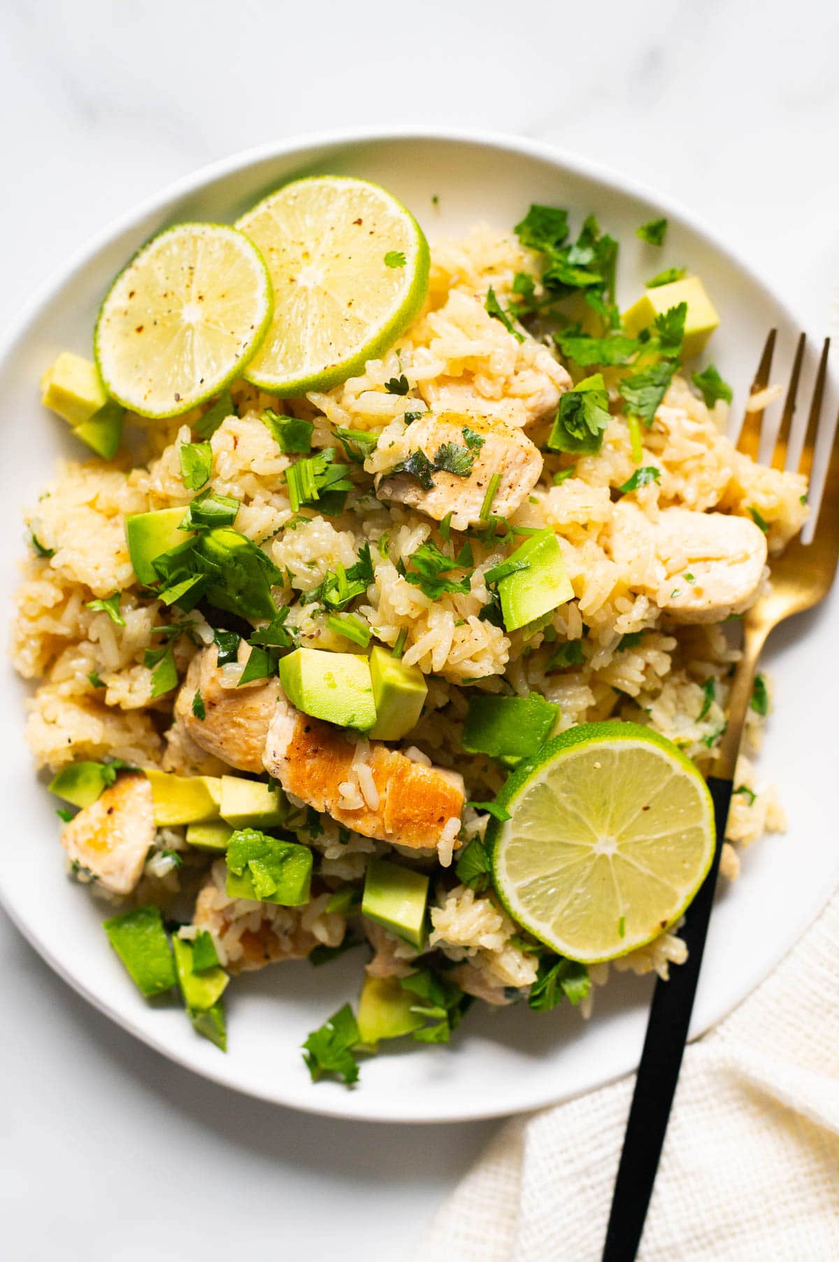 Chicken and rice topped with avocado and limes served on a plate with a fork.