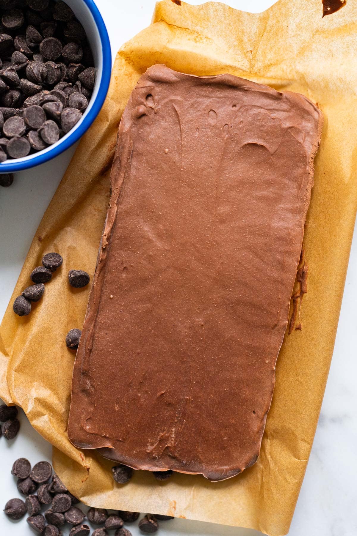 A slab of cottage cheese fudge on parchment paper and chocolate chips around it.