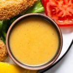 Healthy honey mustard dressing in a bowl. Veggies and chicken strips on a plate.