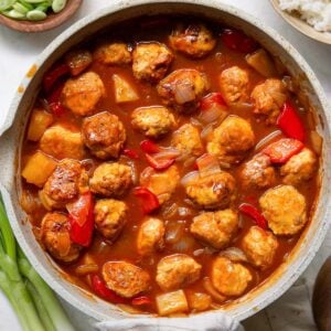 Sweet and sour meatballs with pineapple and bell pepper in a skillet.