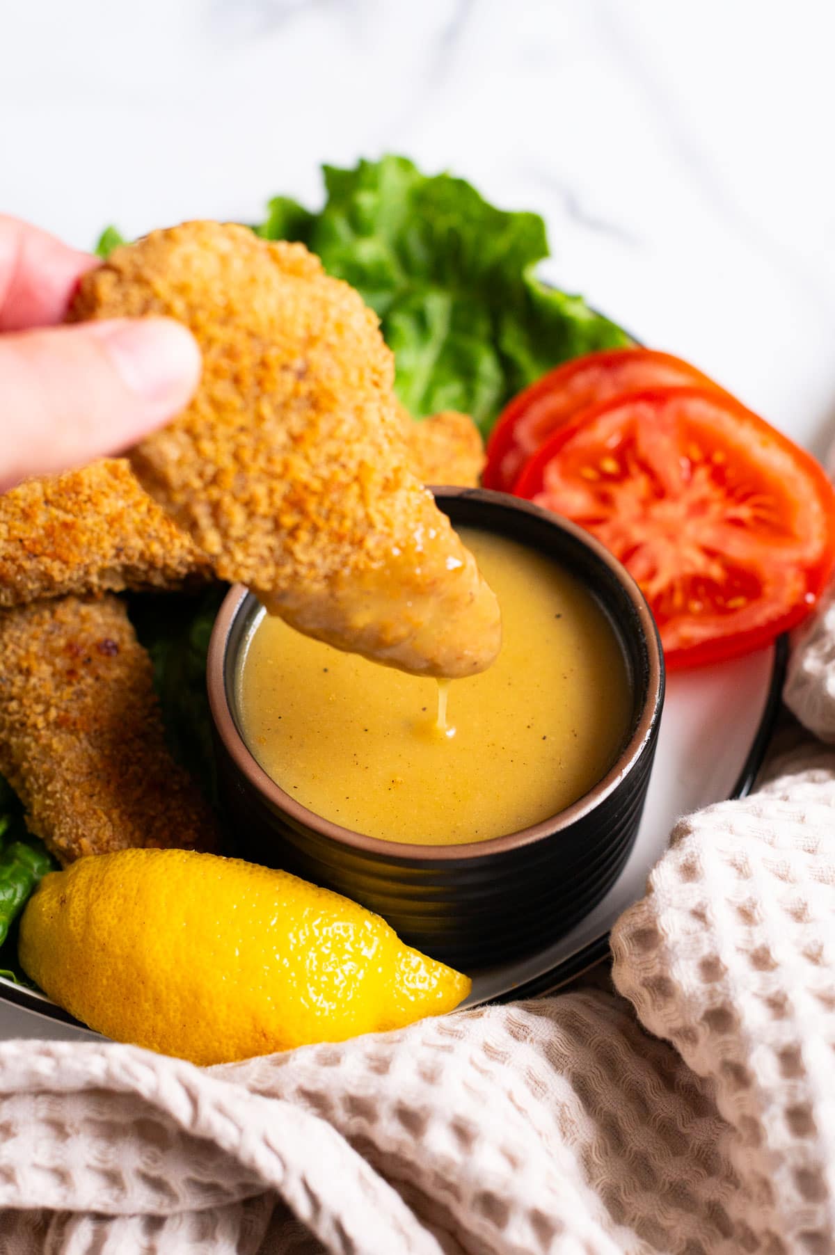 Person dipping a chicken strip into a bowl with honey mustard sauce.