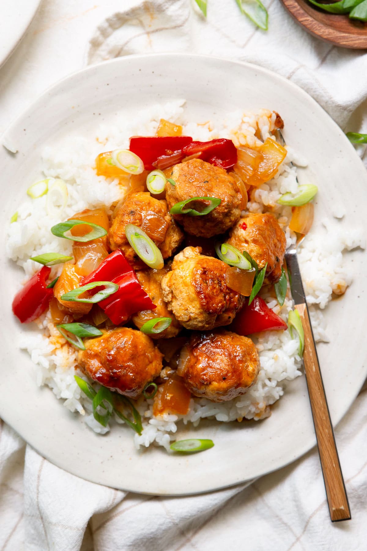 Sweet and sour turkey meatballs with pineapple served on a bed of rice and garnished with green onion.