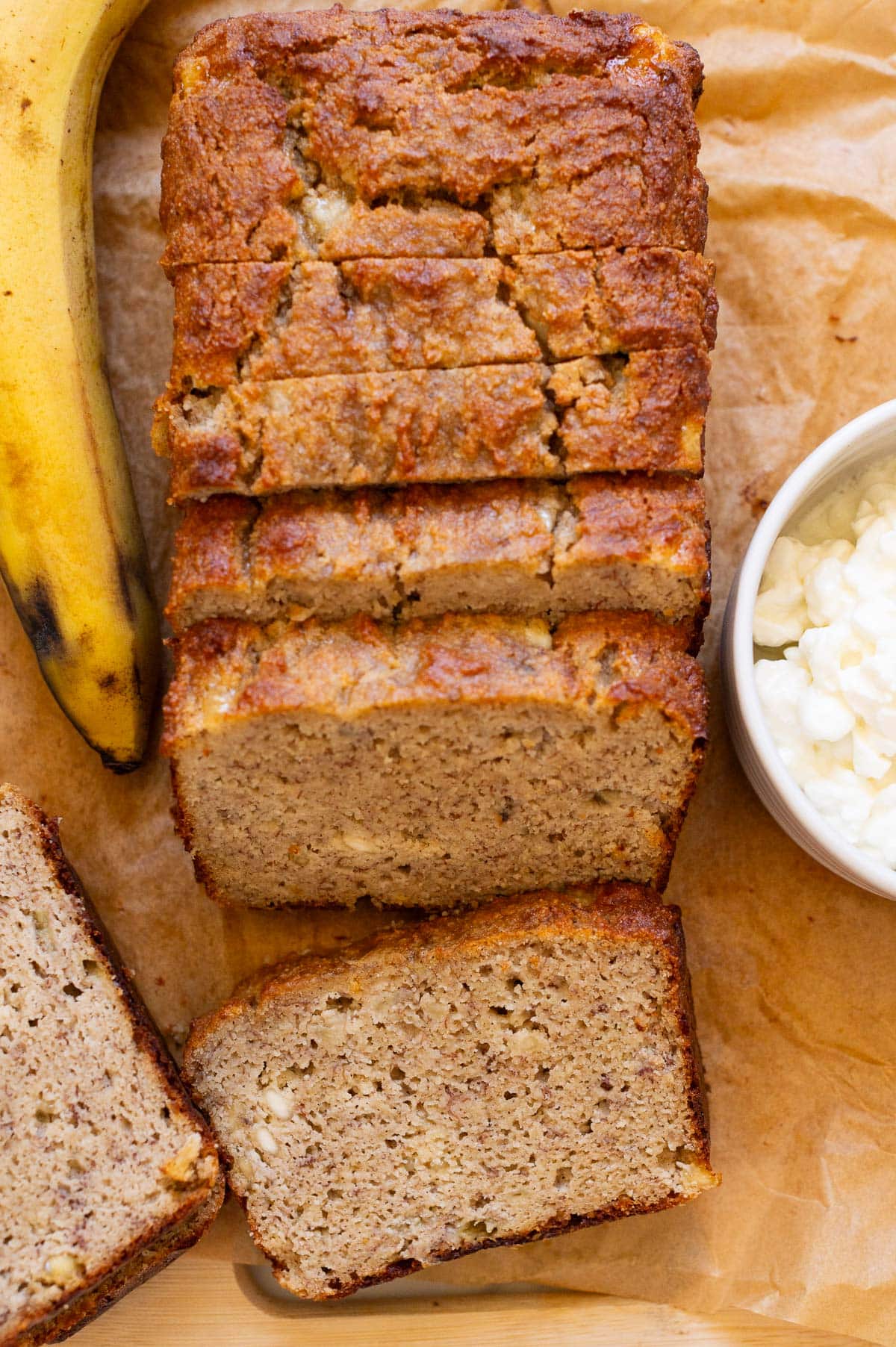 Sliced cottage cheese banana bread on a parchment paper. Cottage cheese in a bowl and bananas.