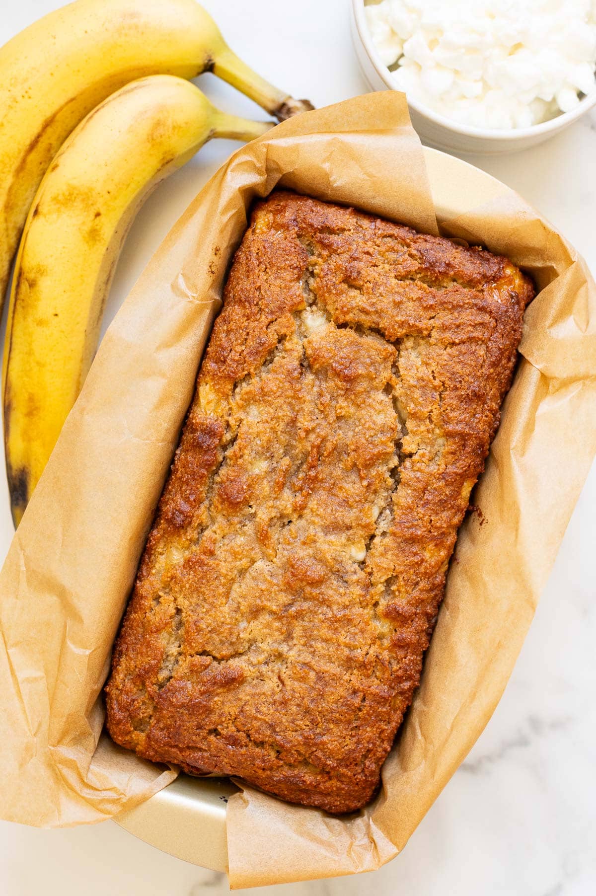 Cottage cheese banana bread in a loaf pan. Bananas and cottage cheese on a counter.