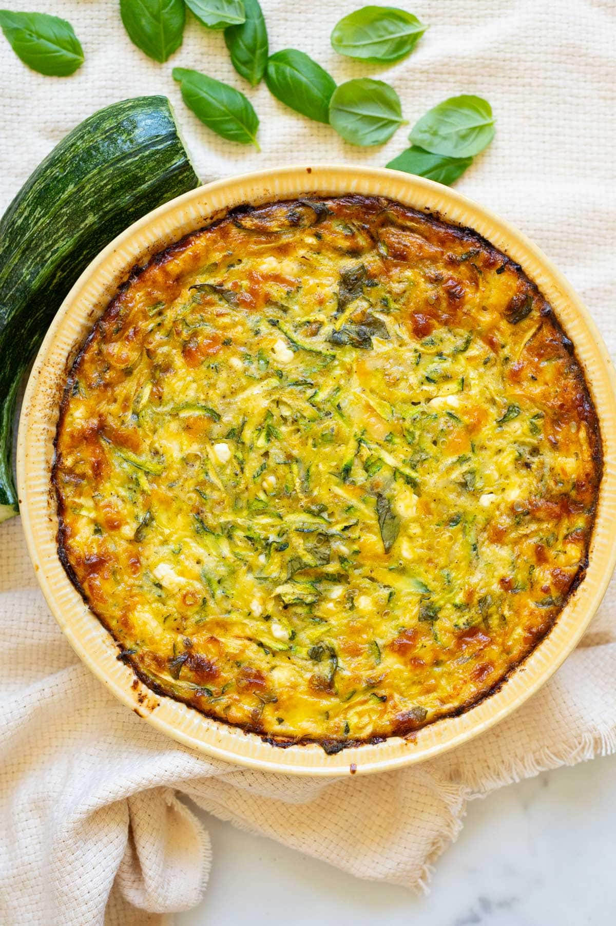 Cottage cheese zucchini quiche in a pie plate. Zucchini and basil on a counter.