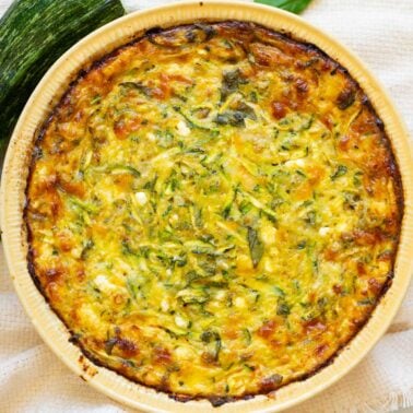 Cottage cheese zucchini quiche in a pie plate. Zucchini and basil on a counter.