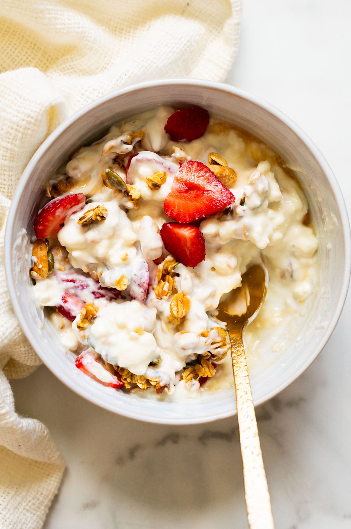 Granola with yogurt, cottage cheese,  and strawberries in a bowl with a spoon.