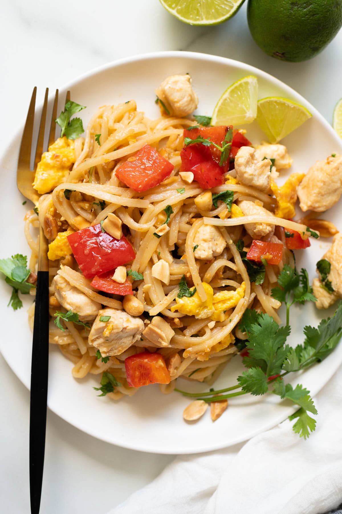 Pad thai with eggs, bell pepper, chicken or my peanuts and cilantro served on a plate with a fork.