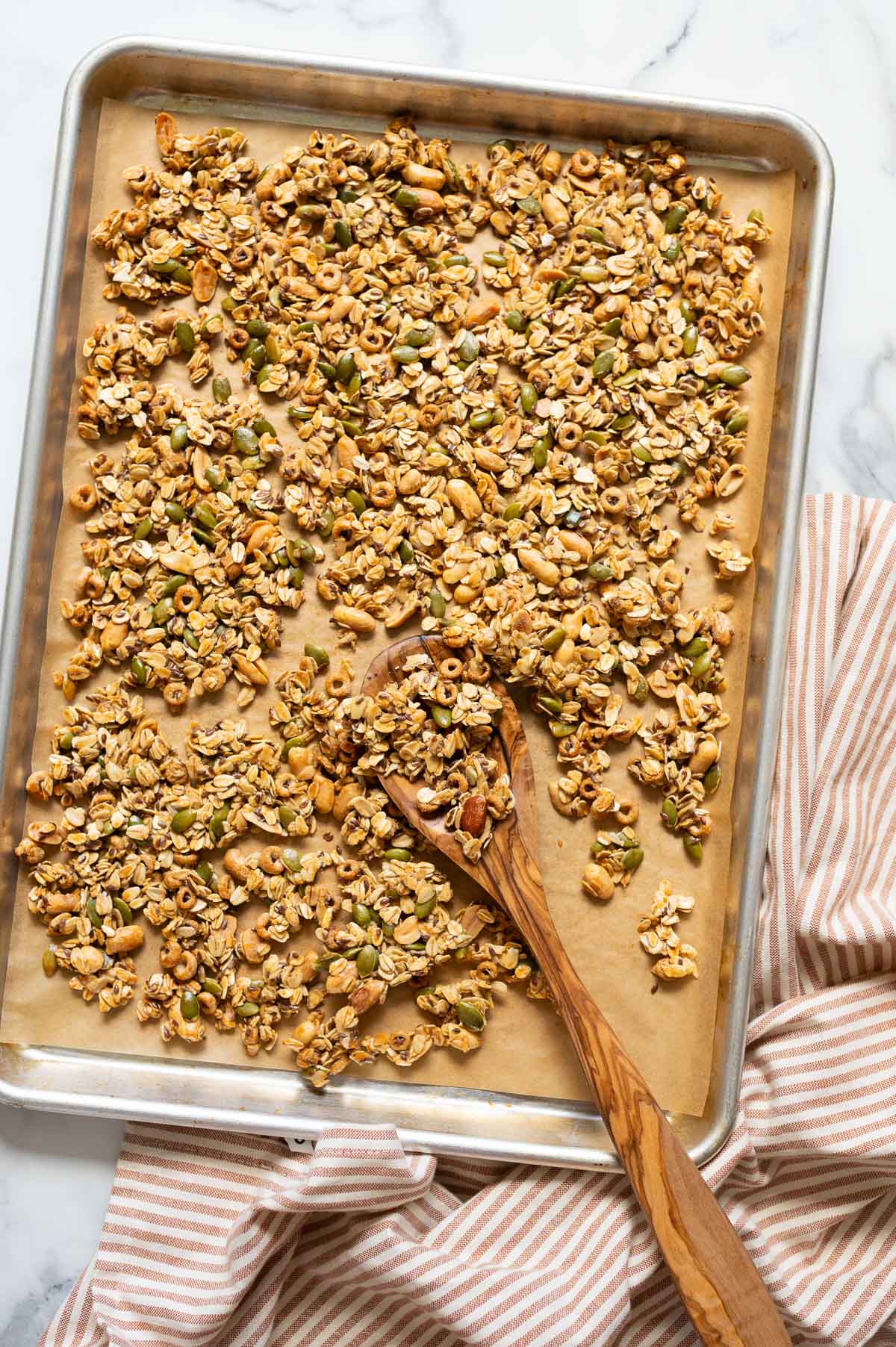 High protein granola on a baking sheet with a wooden spoon. Linen towel on a counter.