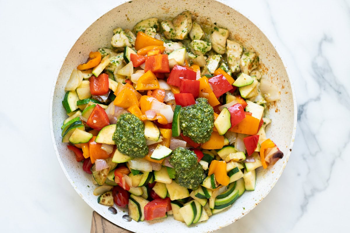 Chicken and veggies sauteed in a skillet with pesto added on top.