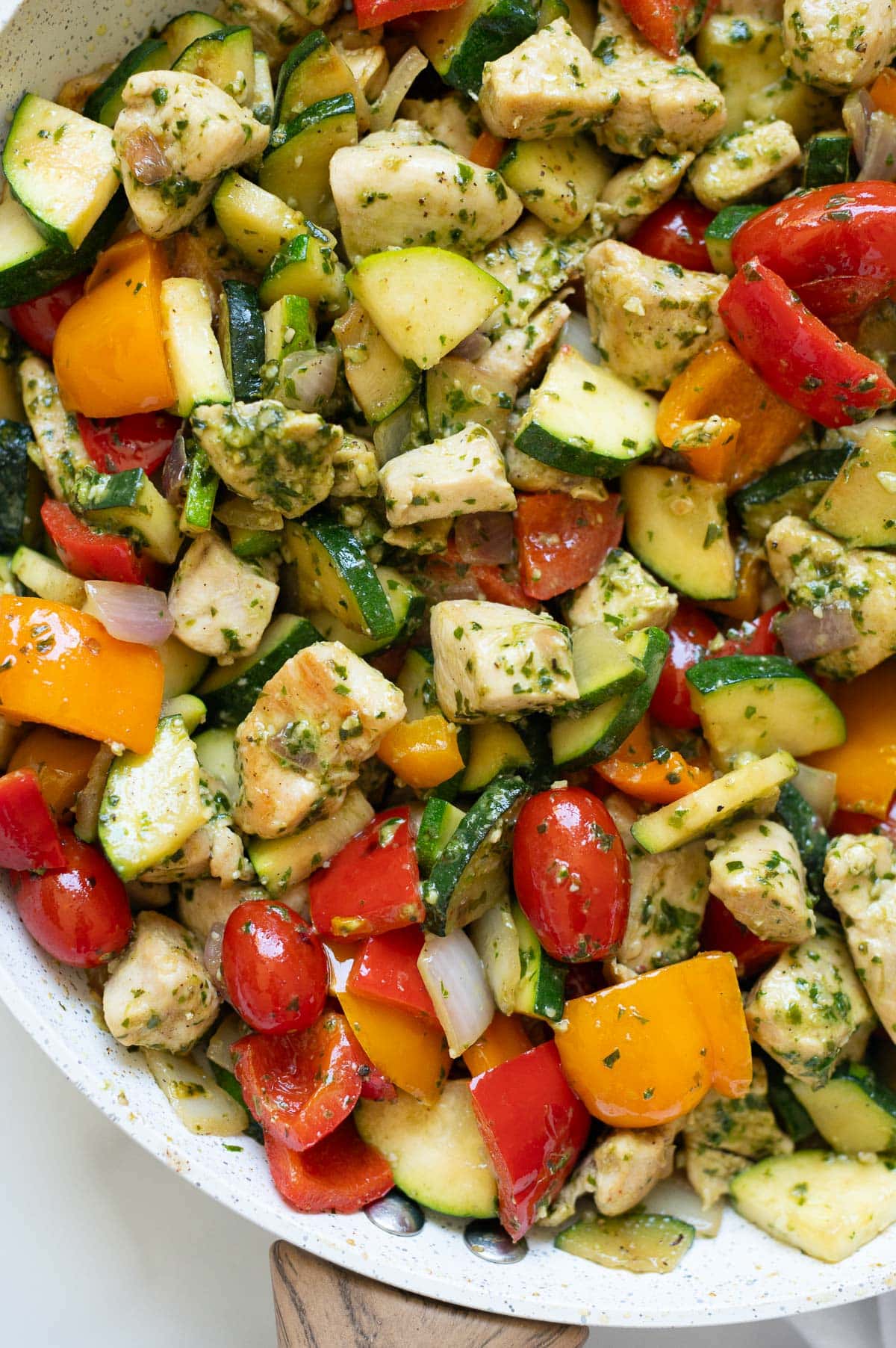 Chicken, bell peppers, zucchini, onion and grape tomatoes in pesto sauce in a skillet.