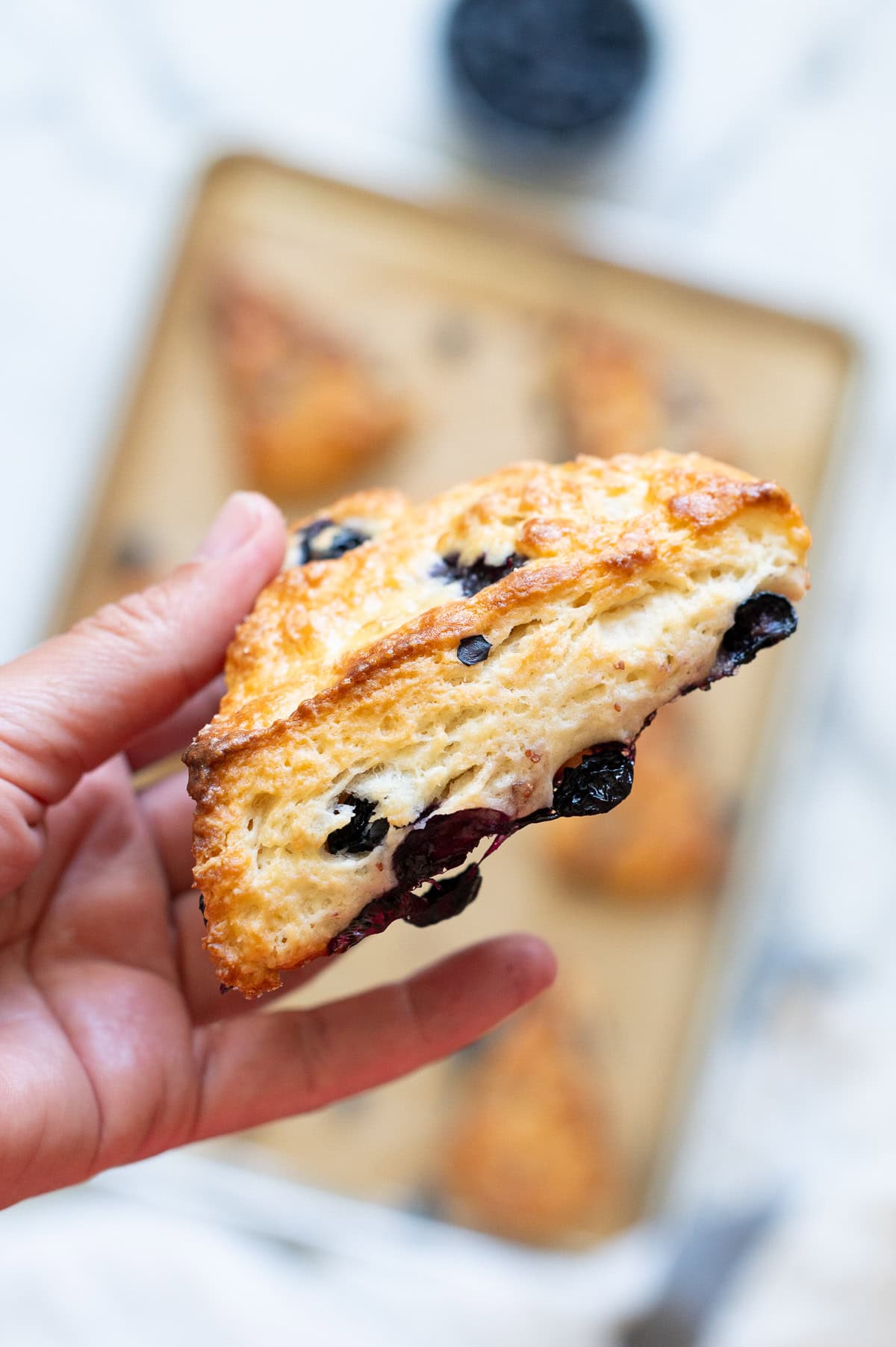 Person holding one blueberry greek yogurt scones above the baking sheet. 