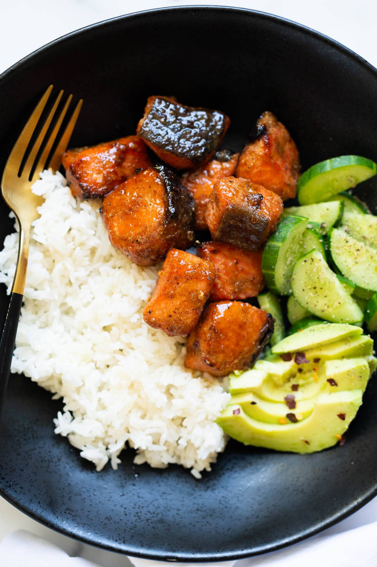 Hot honey salmon served with rice, avocado and cucumber served in a bowl with a fork.