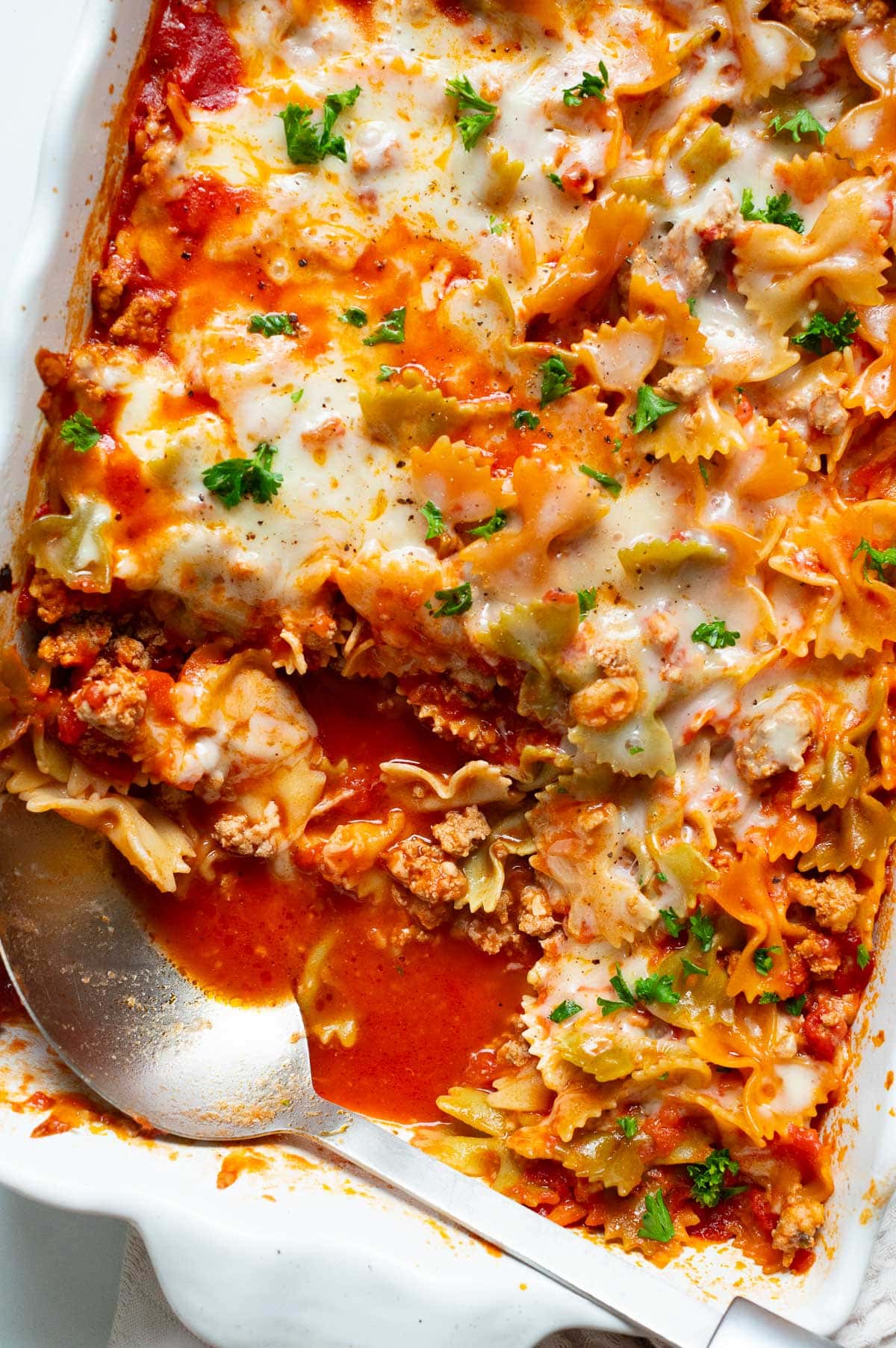 Spoon in a baking dish with pasta and sauce showing texture.