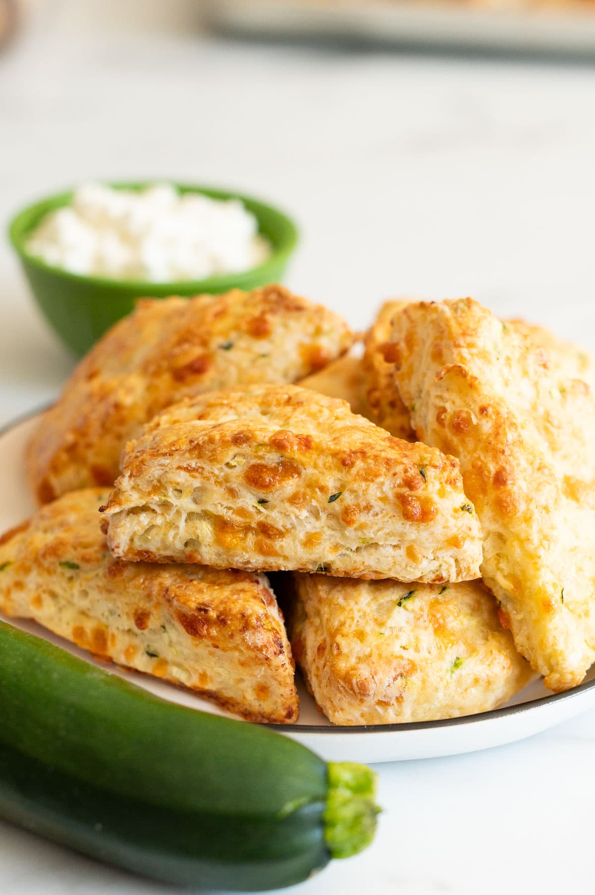 Zucchini cheddar cottage cheese scones on a plate. A bowl with cottage cheese and zucchini on a counter.