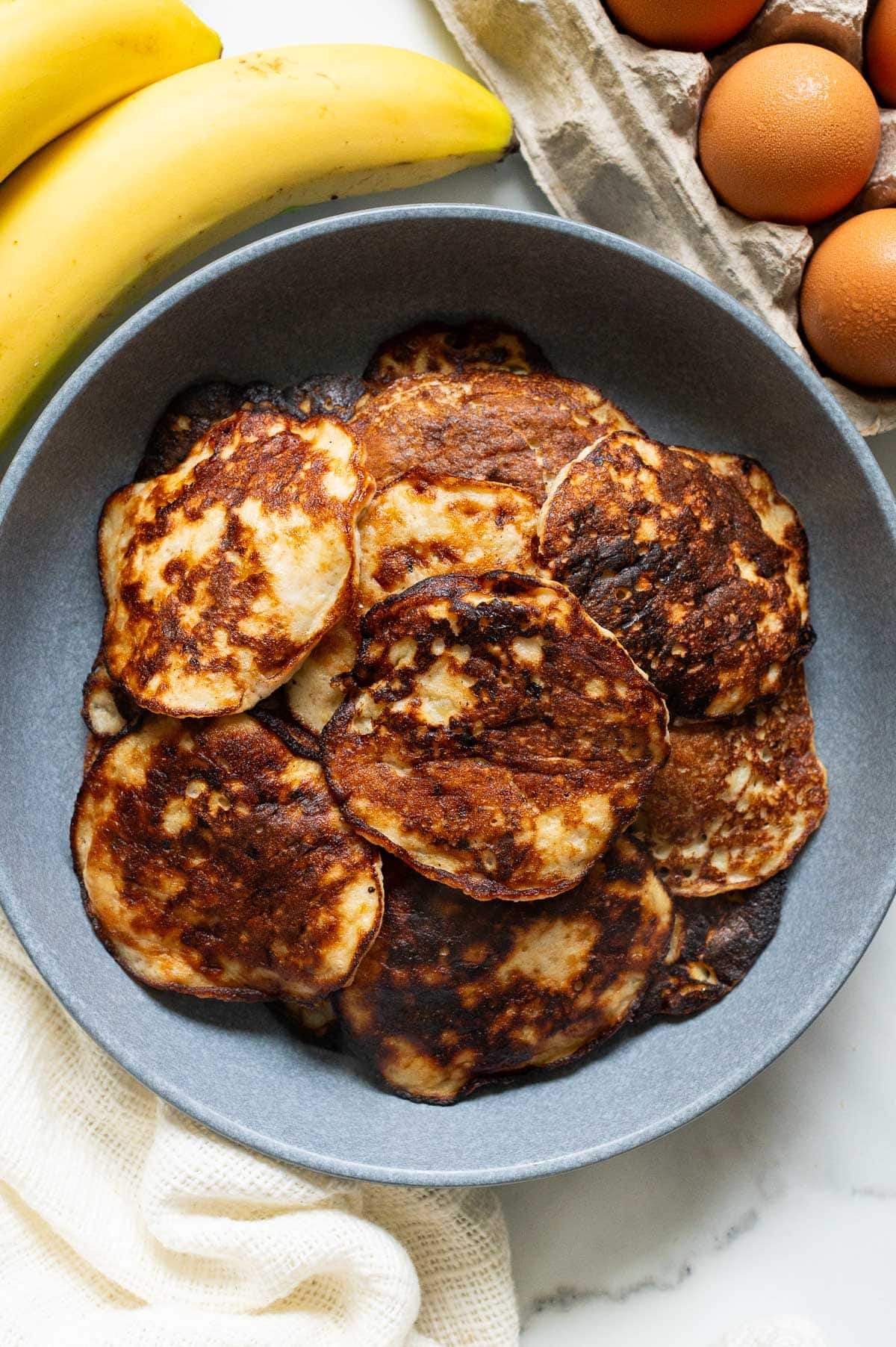 Banana egg pancakes in a bowl. Bananas and eggs on a counter.