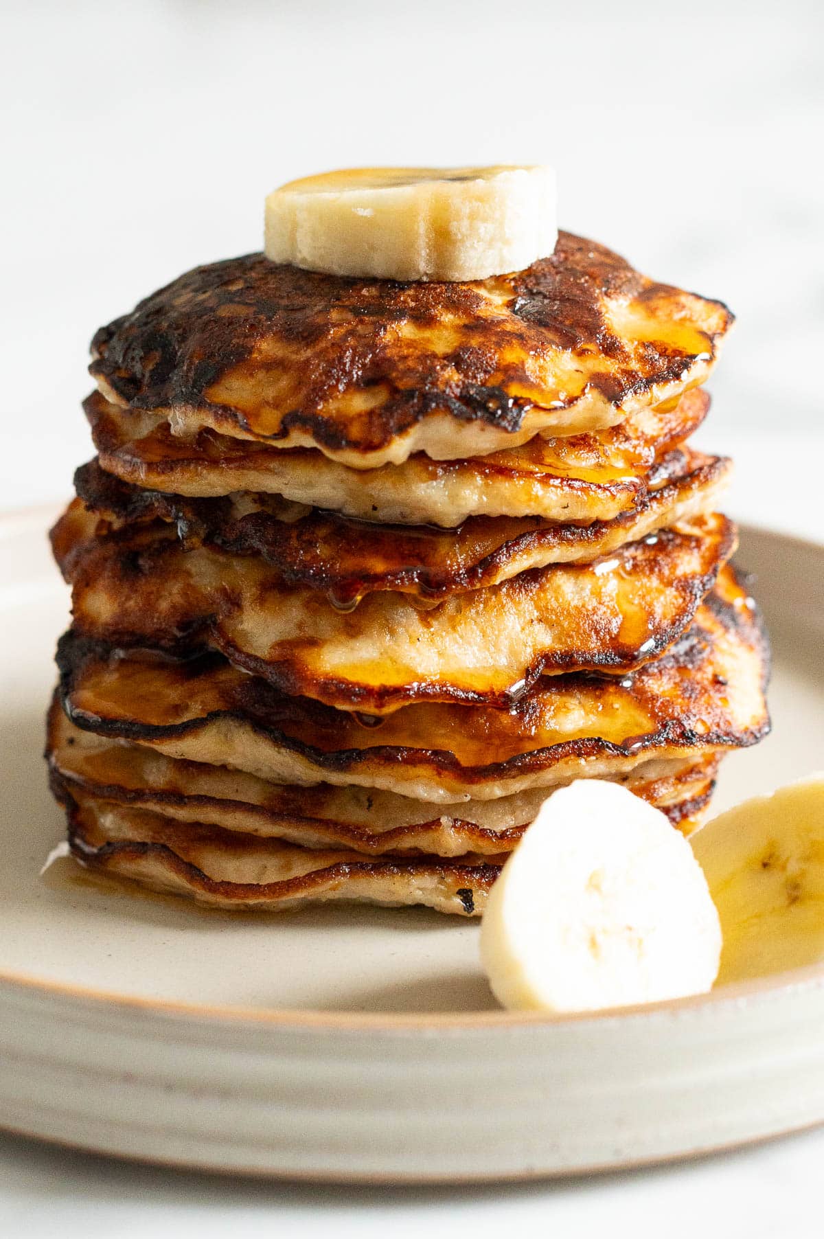 A stack of banana egg pancakes garnished with banana slices and drizzled with maple syrup on a plate.