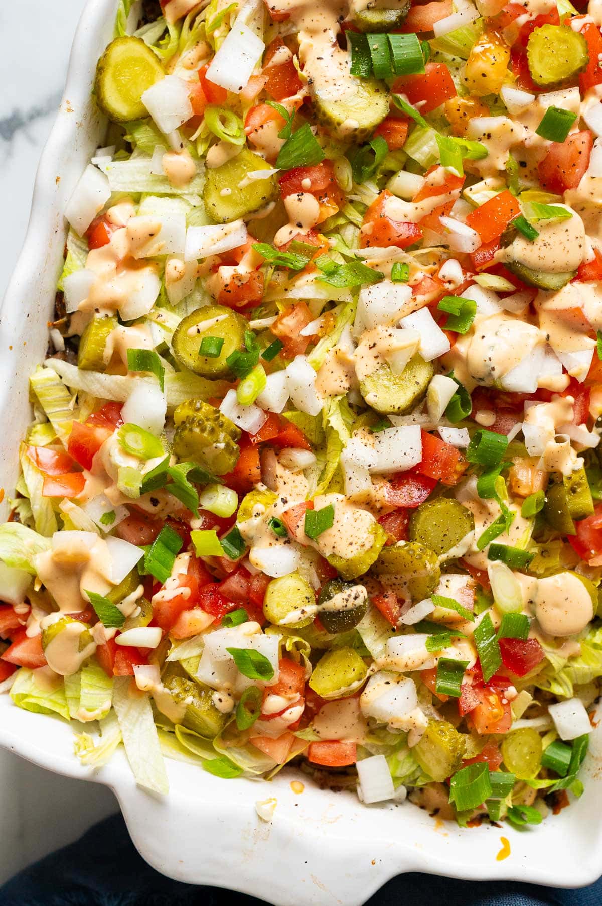 Big Mac casserole with lettuce, pickles, tomatoes and big mac sauce in a baking dish.