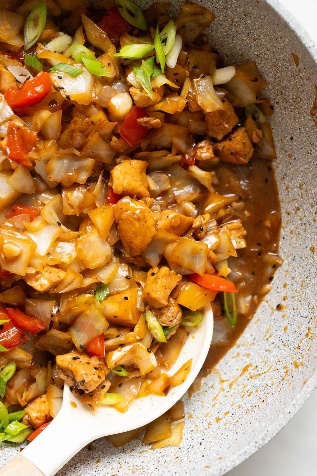 Chicken cabbage stir fry garnished with green onions in a skillet with a spoon.