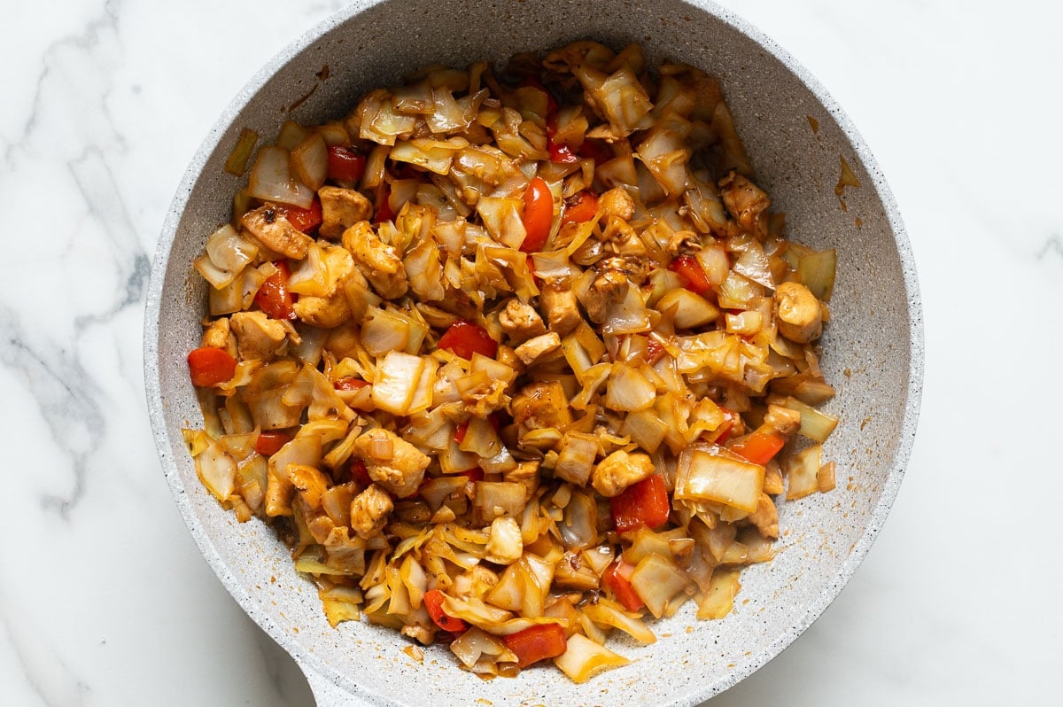 Chicken and cabbage stir fry in a skillet.