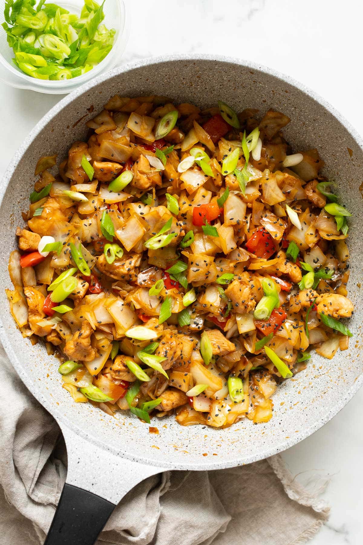 Chicken cabbage stir fry garnished with sesame seeds and green onion in a skillet.