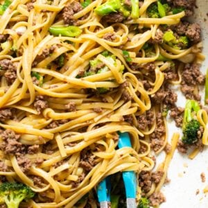 Mongolian ground beef noodles with broccoli in a skillet with tongs.