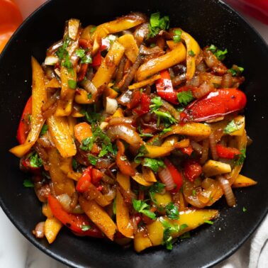 Sauteed peppers and onions garnished with black pepper and parsley.