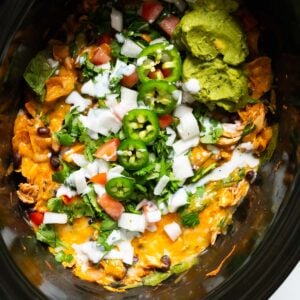 Slow cooker chicken enchilada casserole garnished with cilantro, jalapeno, tomato, white onion and guacamole.