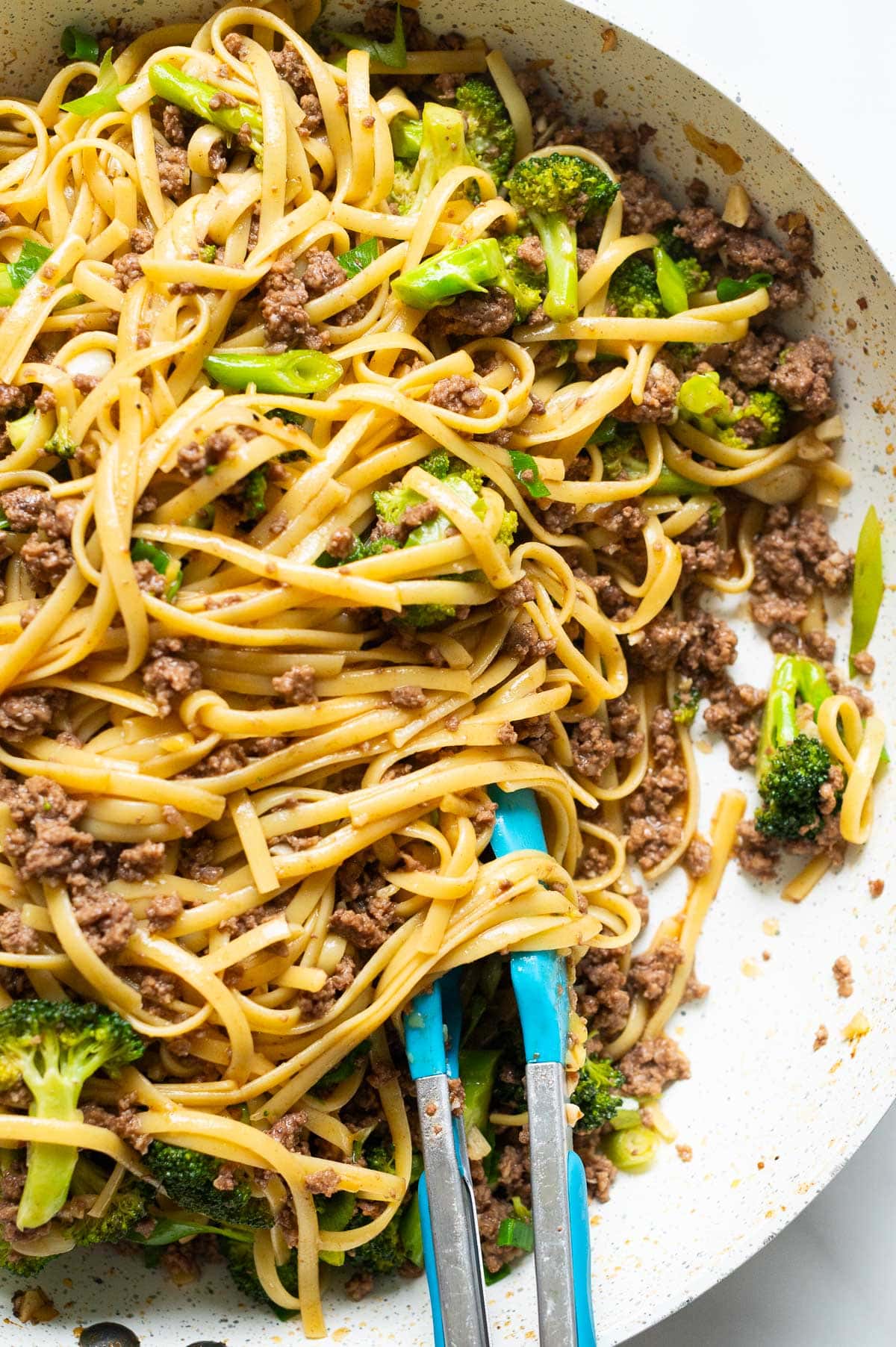 Mongolian ground beef noodles with broccoli in a skillet with tongs.