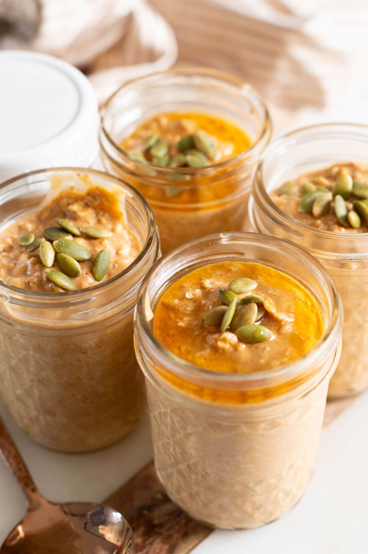 Four jars with protein overnight oats with pumpkin on a kitchen counter.