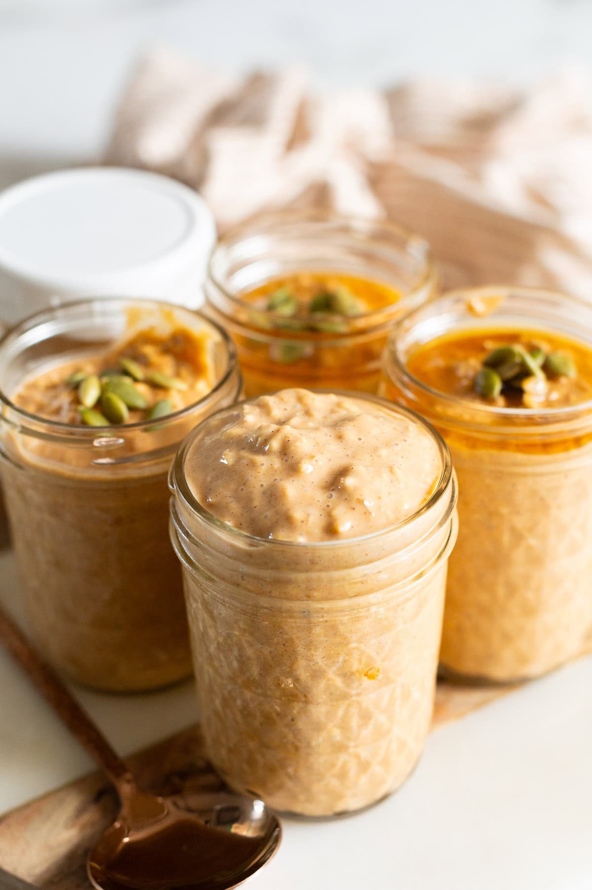 Pumpkin protein overnight oats topped with pumpkin seeds and maple syrup in glass jars.