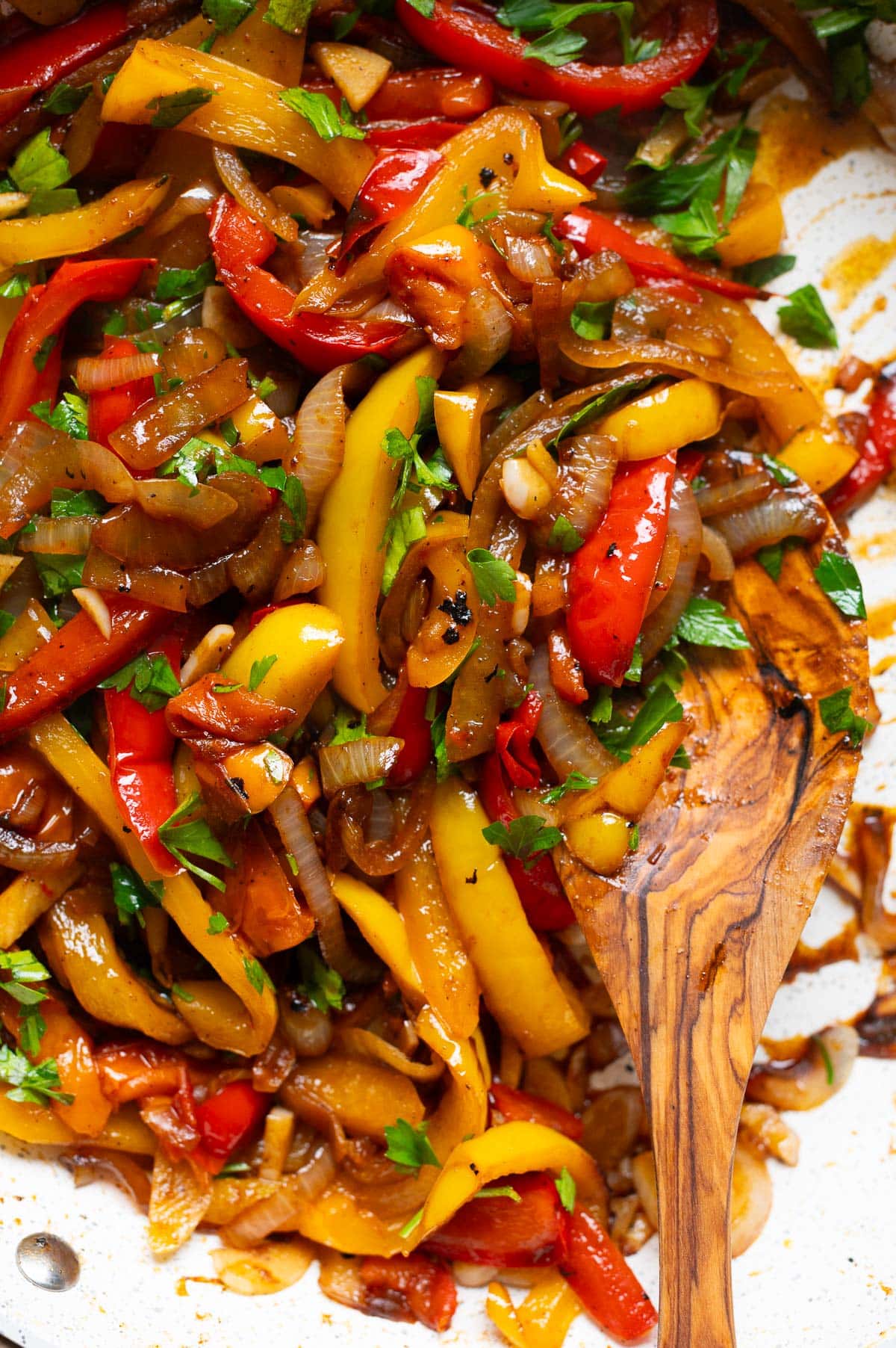 Sauteed peppers and onions garnished with parsley and scooped with a wooden spoon.