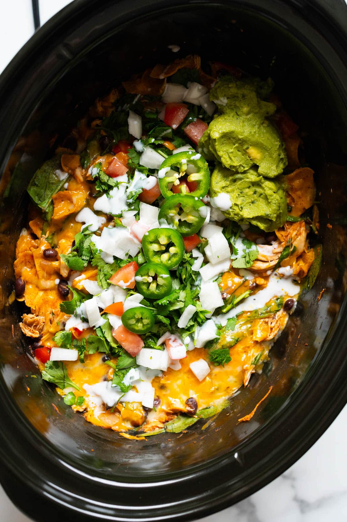 Slow cooker chicken enchilada casserole garnished with cilantro, jalapeno, tomato, white onion and guacamole.