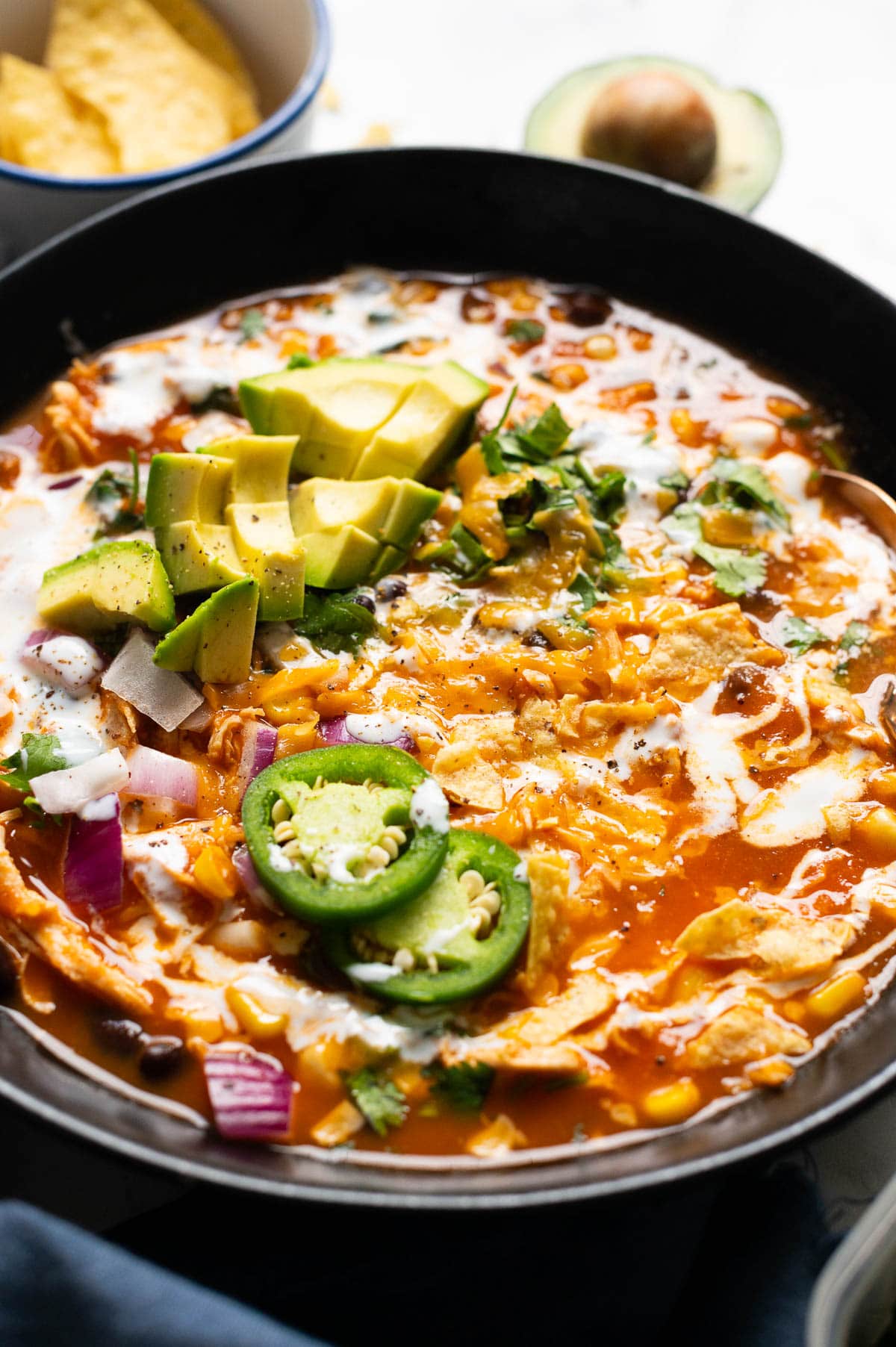 Side view of creamy chicken enchilada soup with garnishes in a bowl.