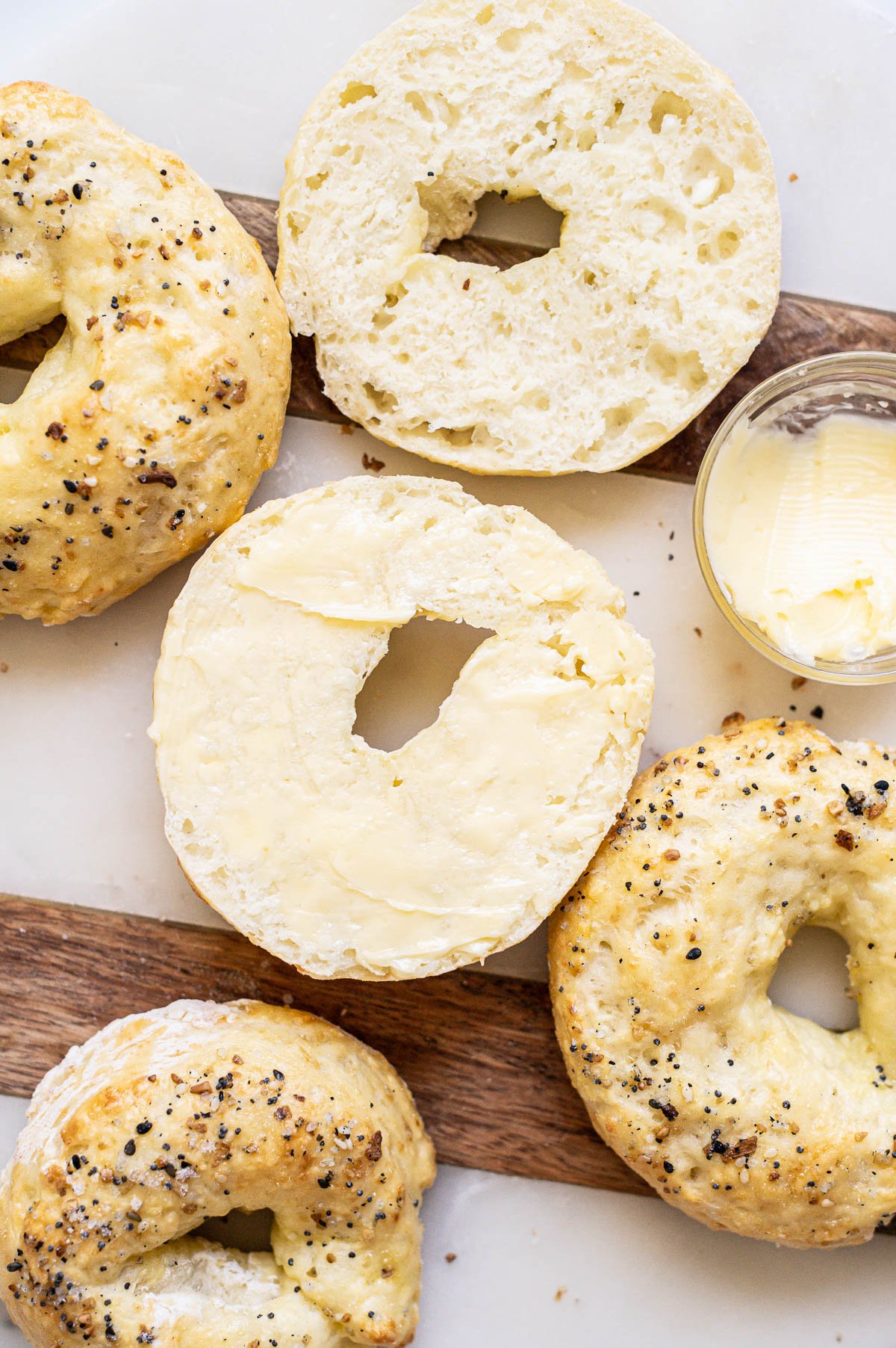 Sliced cottage cheese bagel spread with butter. More bagels around it on a board.