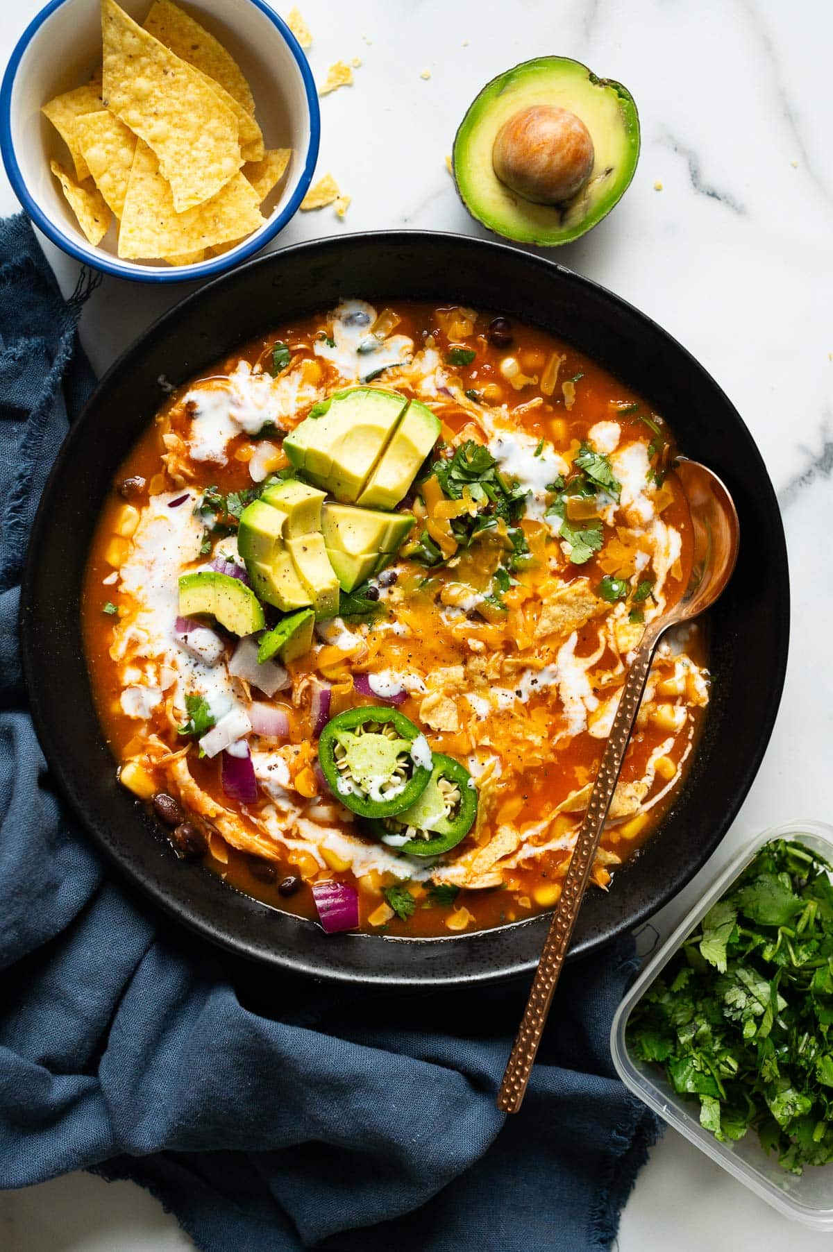 Creamy chicken enchilada soup garnished with avocado, cilantro, red onion and jalapeno served in a bowl.