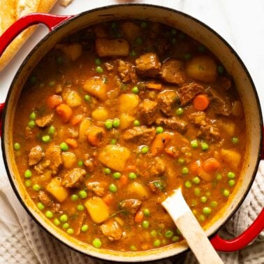 Beef stew in a pot with wooden spoon.