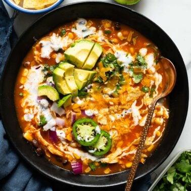 Creamy chicken enchilada soup garnished with avocado, cilantro, red onion and jalapeno served in a bowl.