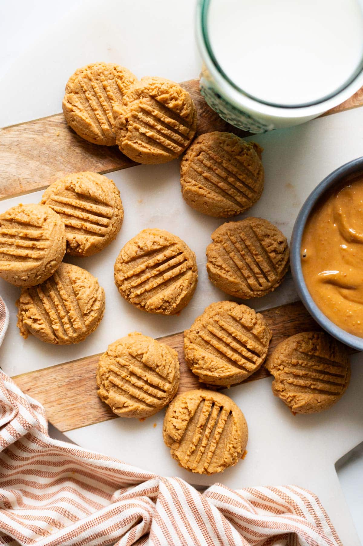 2 ingredient peanut butter cookies on a tray. Peanut butter in a bowl and milk in a glass.