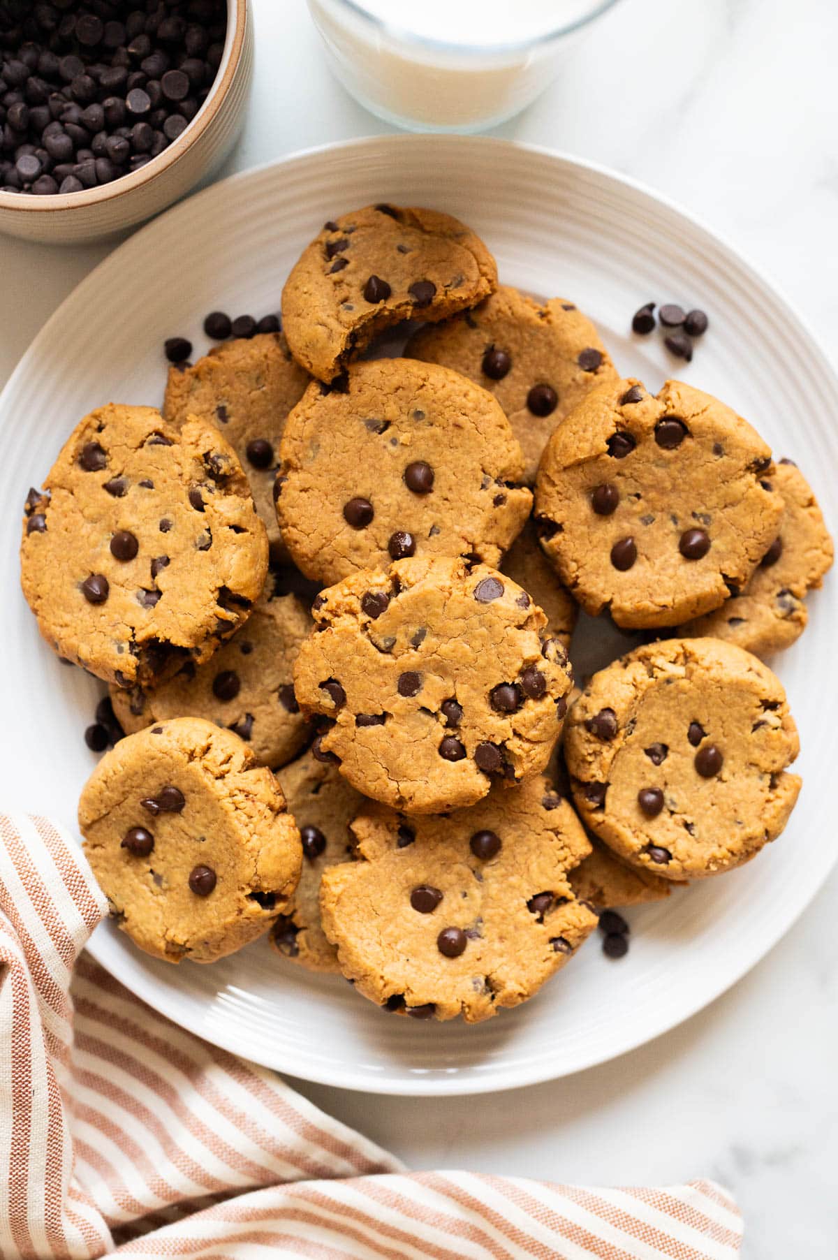 3 ingredient peanut butter cookies on a plate. Chocolate chips in a bowl and milk in a glass.